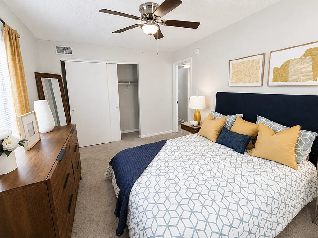 Inviting bedroom with modern decor, featuring a cozy bed with geometric-patterned duvet, stylish wooden dresser, and a chic ceiling fan for comfort.