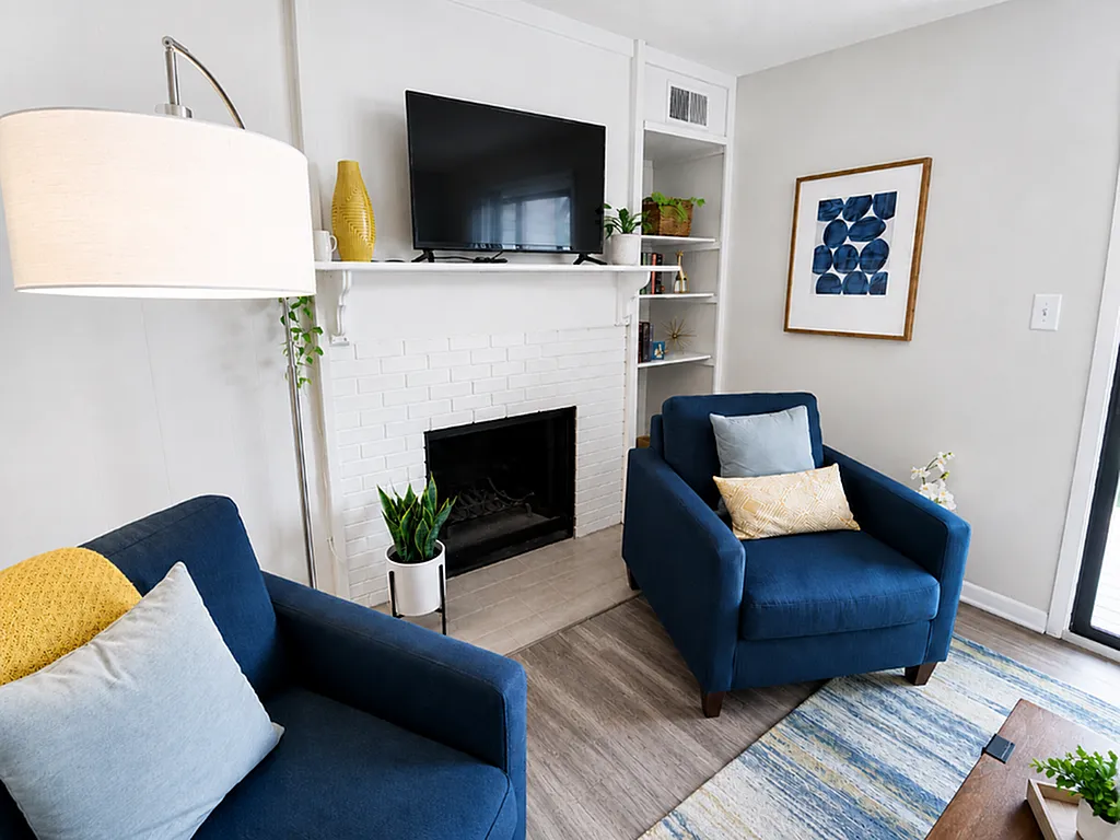 Cozy living room featuring stylish blue armchairs, a modern white brick fireplace, and tasteful decor creating a welcoming ambiance.