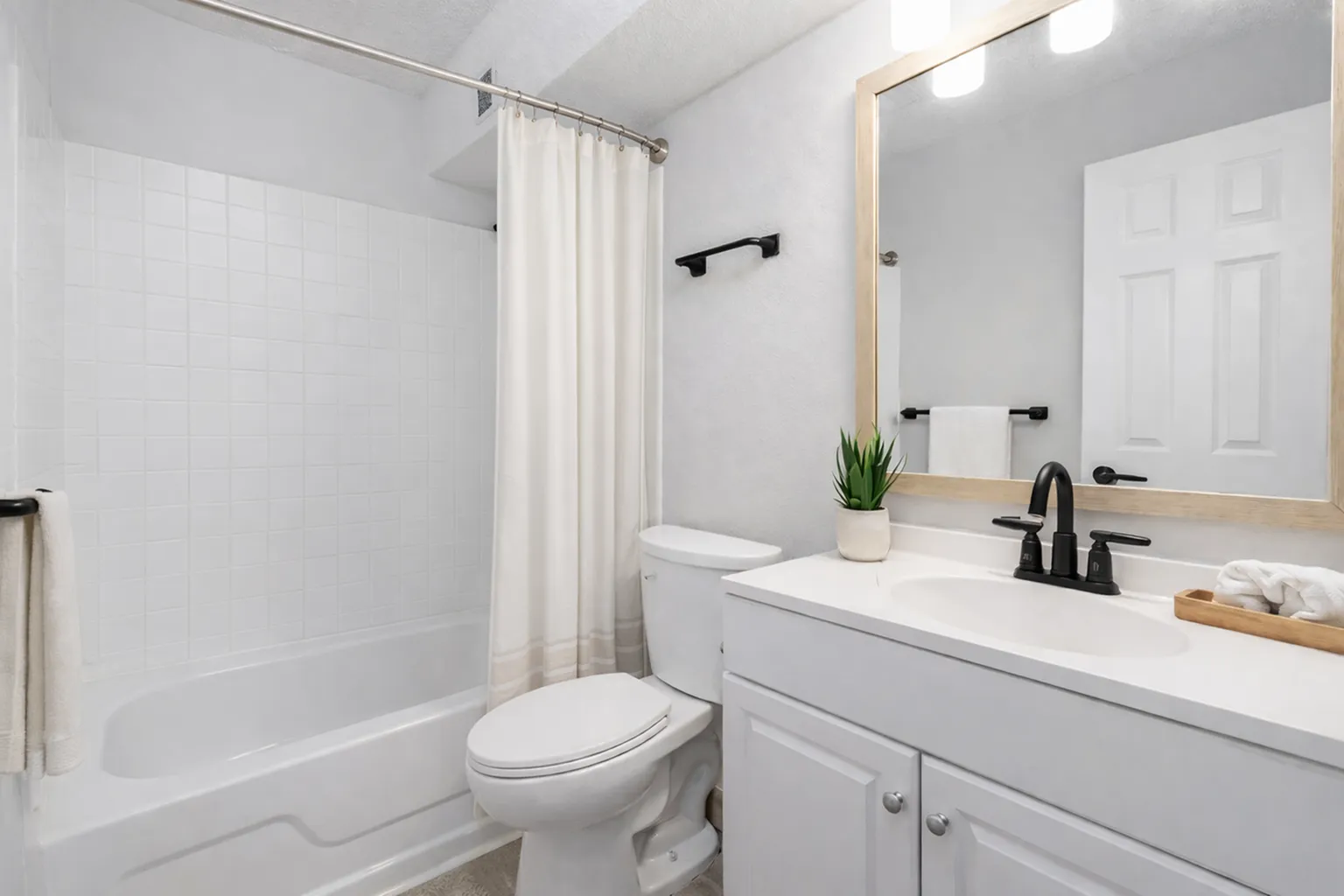 Elegant modern bathroom with sleek white cabinetry, stylish black fixtures, and a large mirror, complemented by a lush green plant for a refreshing touch.