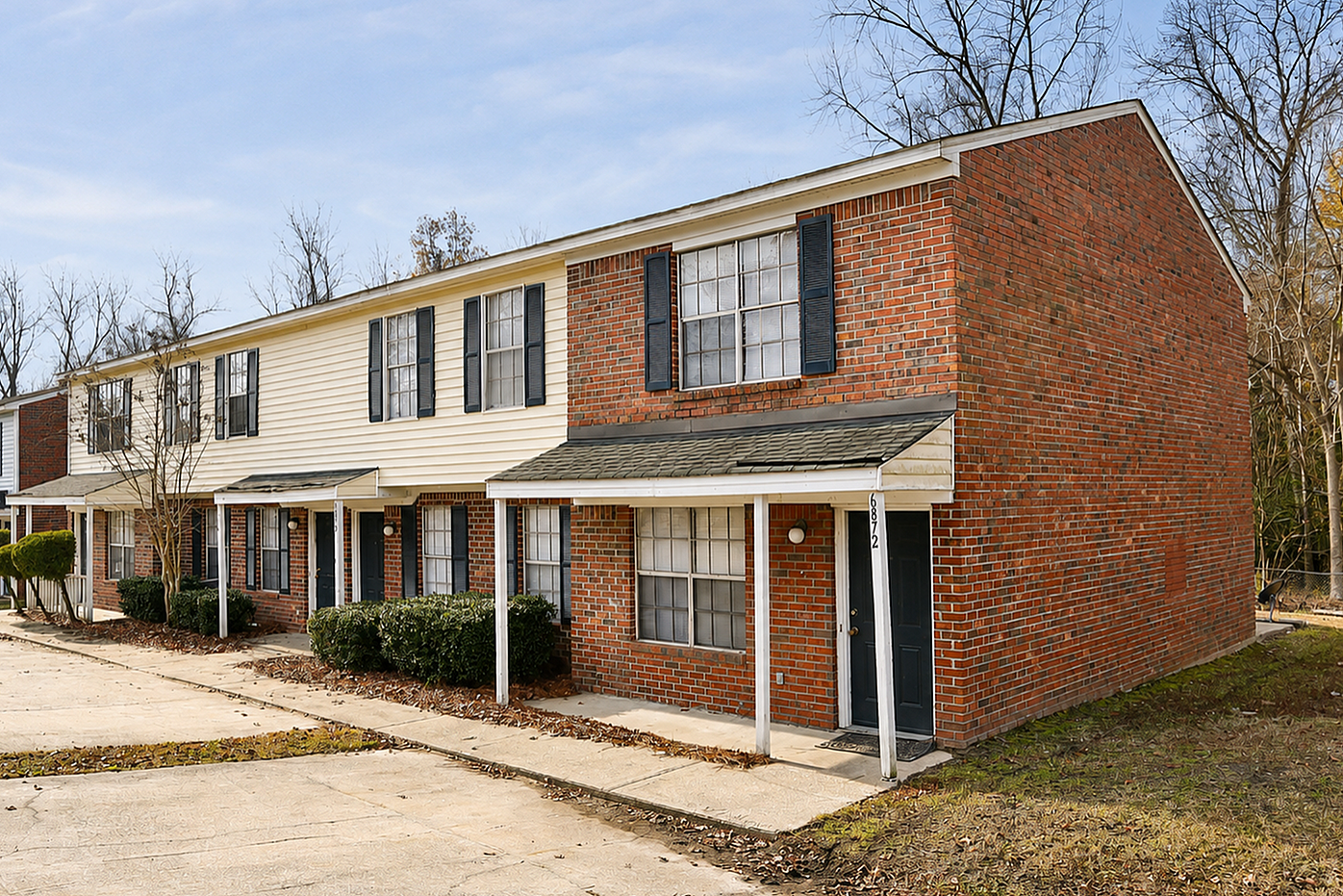 Charming townhouse exterior with classic brick facade, inviting front porch, and ample parking space in a peaceful neighborhood setting.
