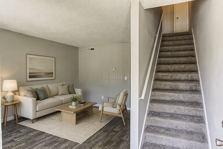 Inviting living room with modern decor, plush sofa, and natural light, adjacent to a carpeted staircase in a cozy apartment.