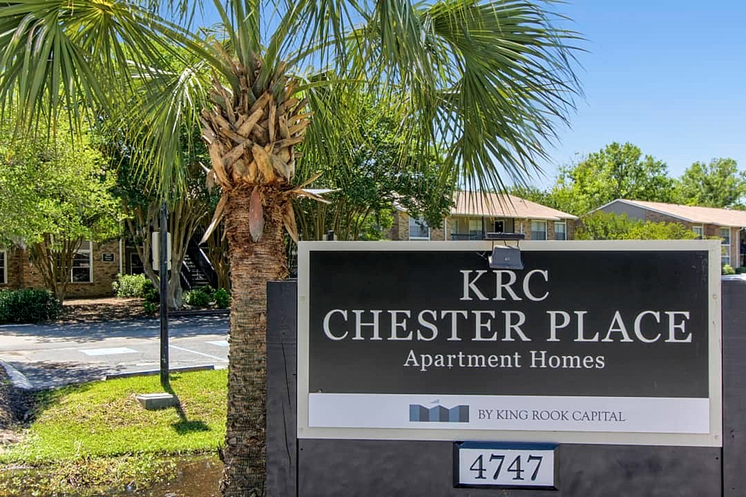 Inviting entrance sign for KRC Chester Place Apartment Homes, surrounded by lush greenery and a charming palm tree, highlighting the welcoming and serene atmosphere.
