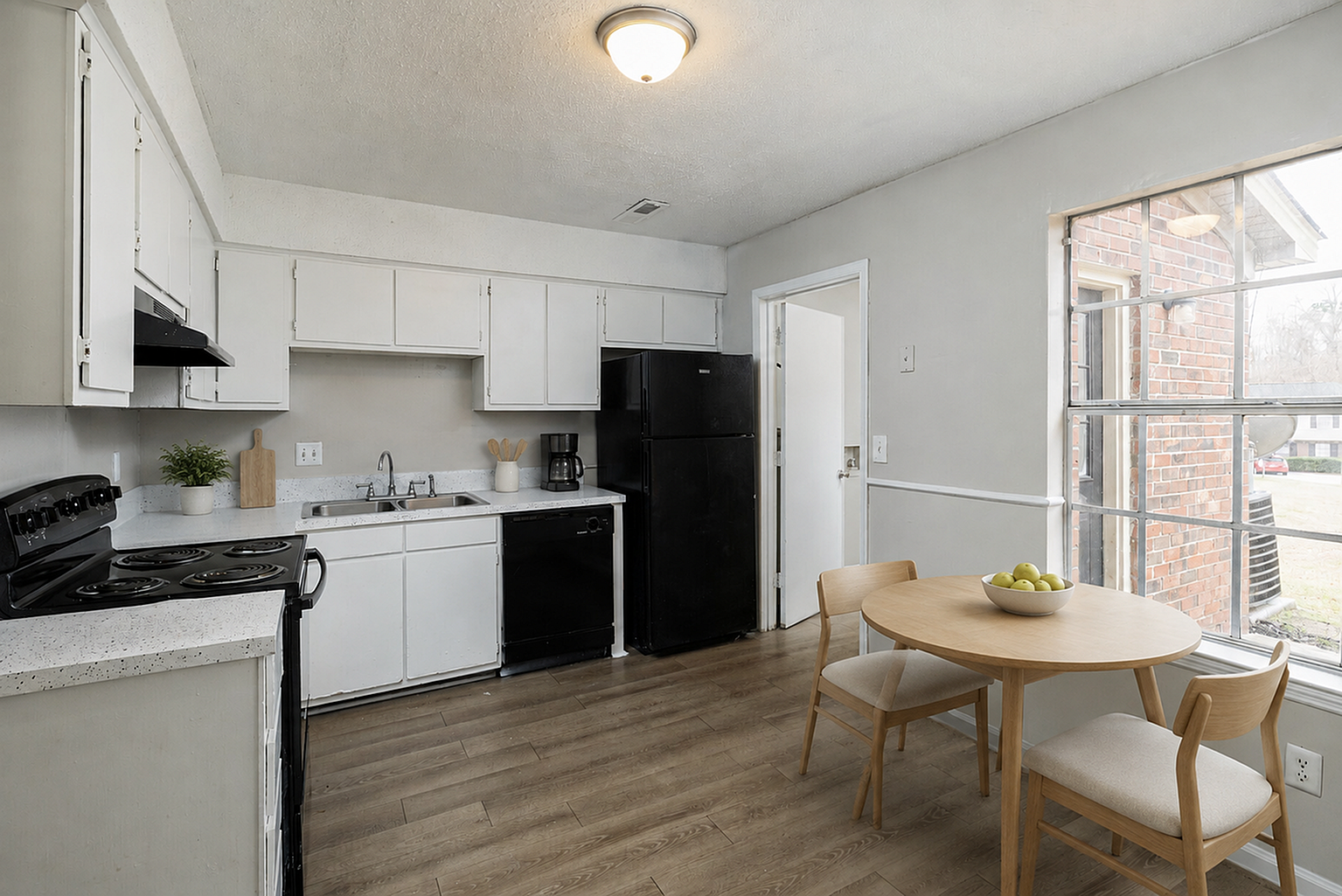 Bright and welcoming kitchen with modern black and white appliances, sleek countertops, and a cozy dining area by a large window.