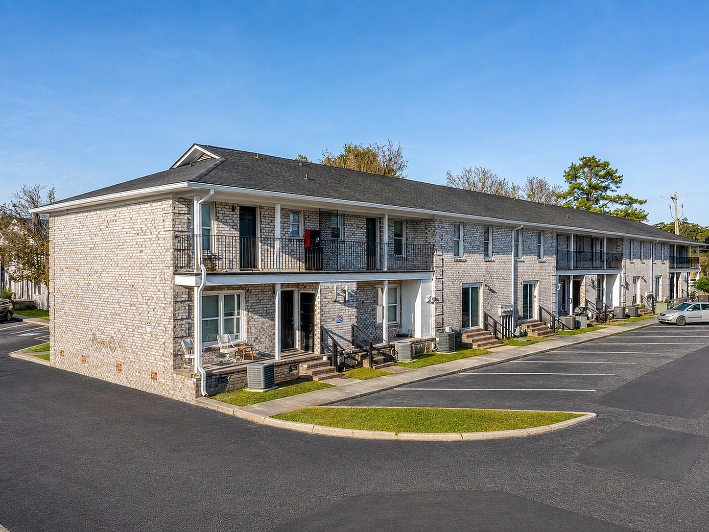 Elegant two-story apartment complex with brick exterior, featuring private balconies and ample parking space in a serene neighborhood.