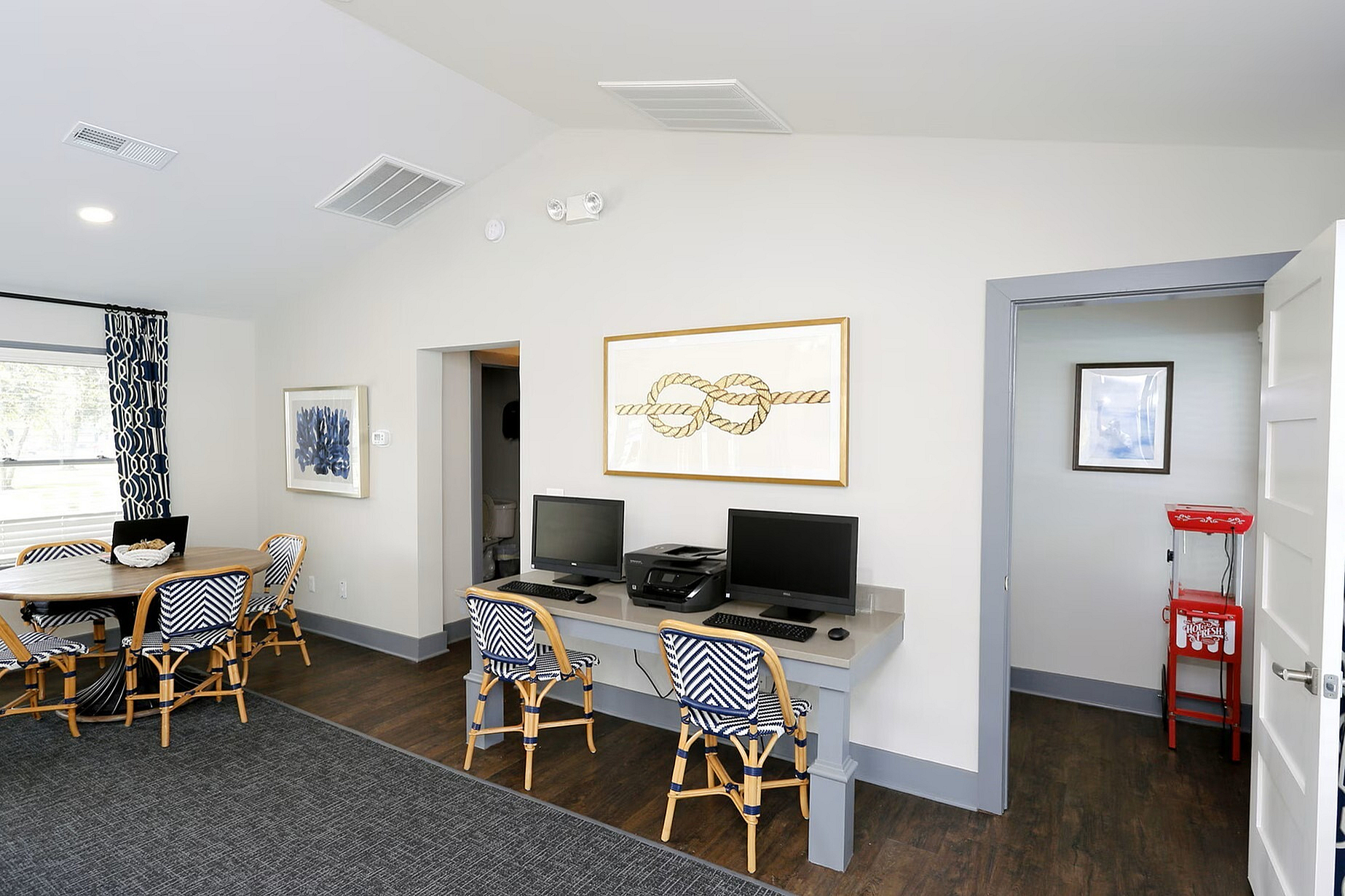Chic common area with modern decor, featuring a work desk with computers, stylish dining table, and vibrant art pieces, perfect for socializing and productivity.