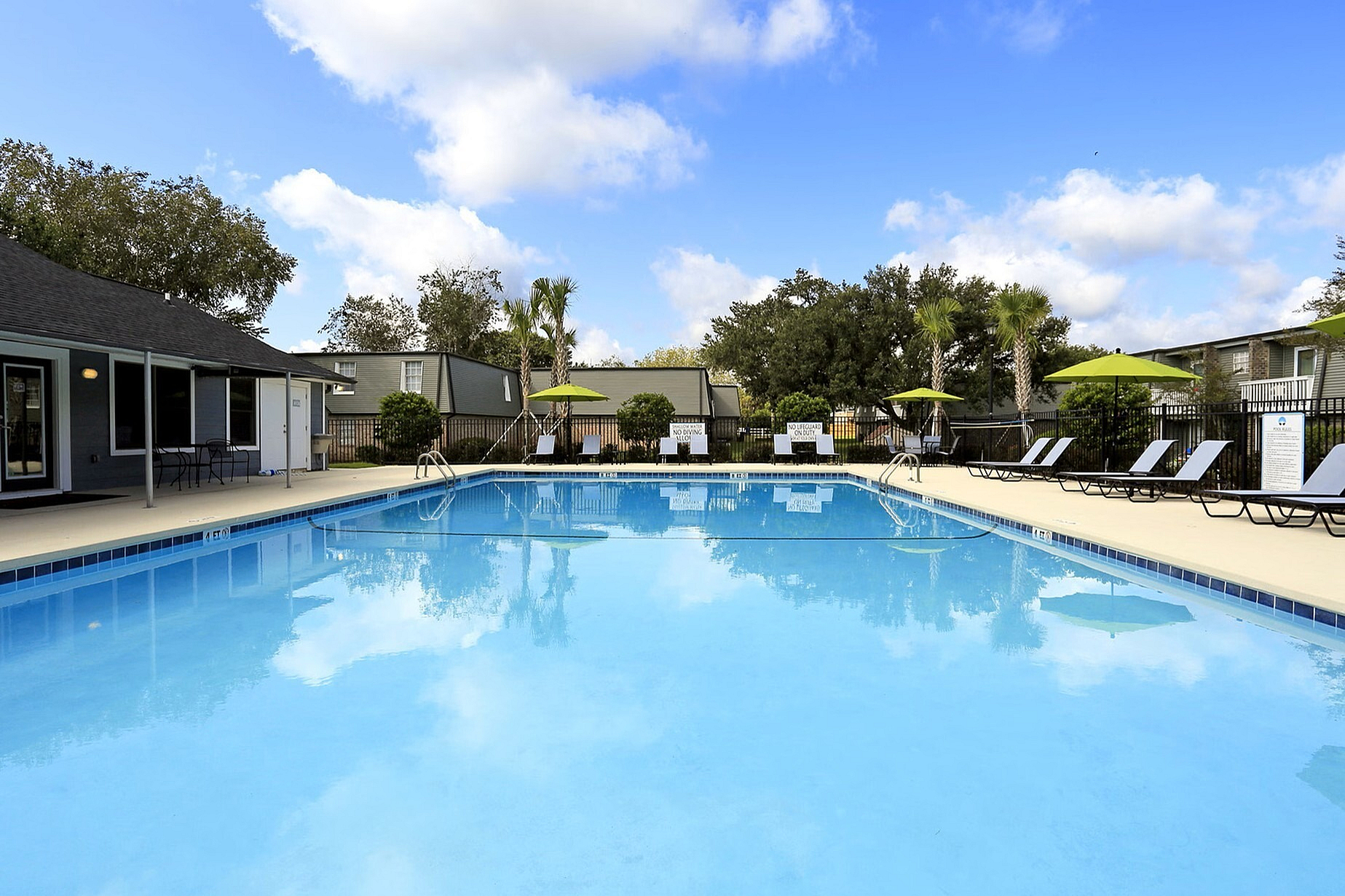 Inviting outdoor pool area with lounge chairs, surrounded by lush greenery and a bright blue sky.