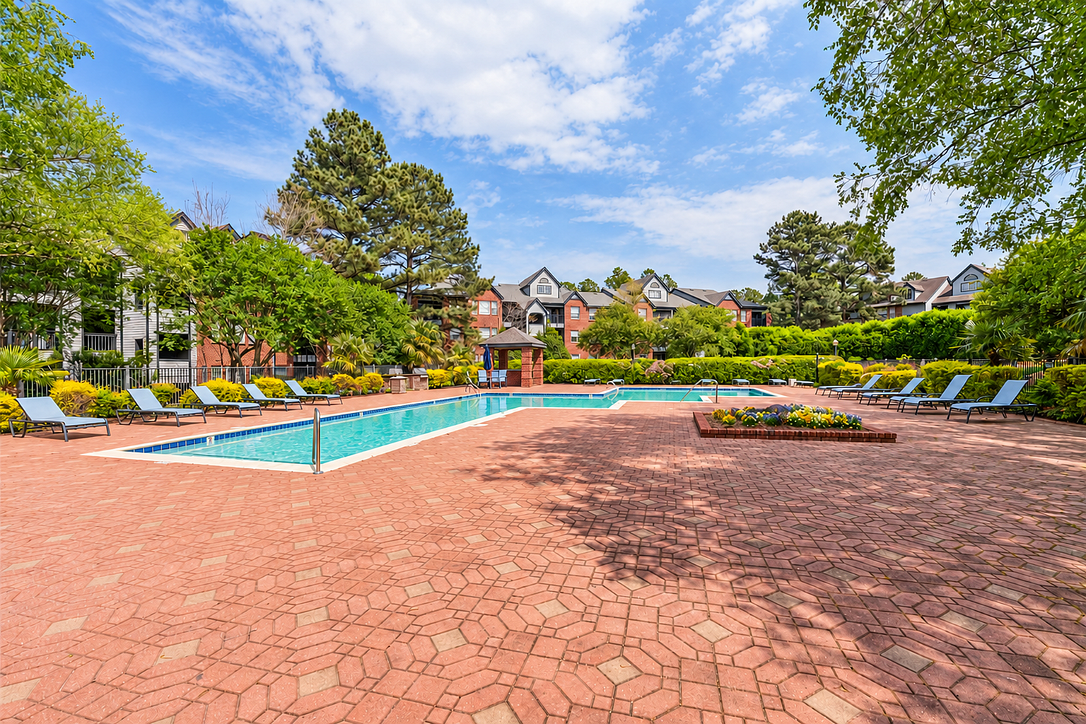 Luxurious outdoor pool area with stylish lounge chairs, surrounded by lush greenery and elegant apartment buildings.
