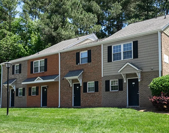 Charming brick townhouse with a well-maintained lawn and lush green surroundings.