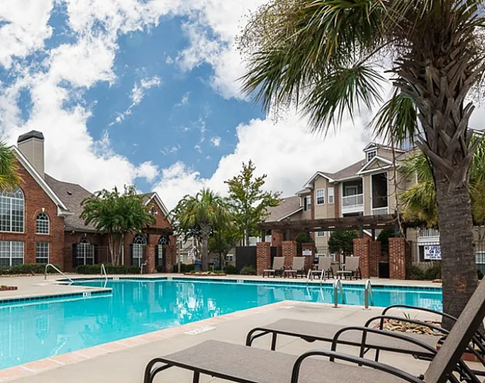 Inviting apartment pool area with lounge chairs and palm trees under a blue sky.
