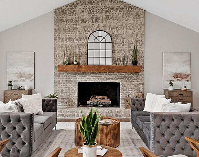 Chic living room with stylish grey tufted sofas, wooden coffee tables, and a modern brick fireplace.