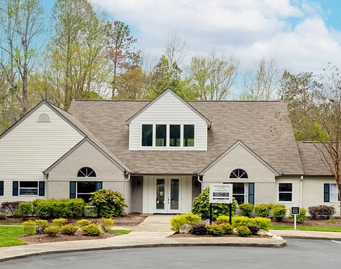 Picturesque suburban home with a gabled roof, surrounded by lush greenery and clear skies.