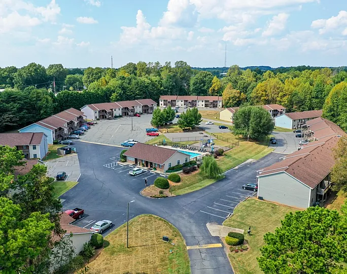 Aerial view of a serene residential community surrounded by lush greenery, with well-maintained roads and parking facilities.