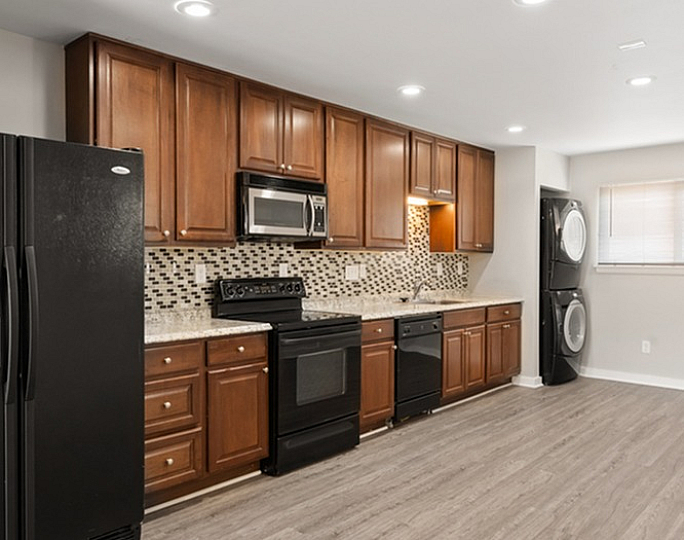 Modern kitchen with sleek wooden cabinets, black appliances, and elegant mosaic backsplash.