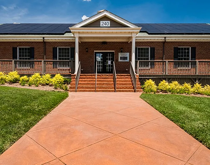 Inviting entrance of a brick building with a well-maintained pathway, steps leading up to a porch, and a clear blue sky.