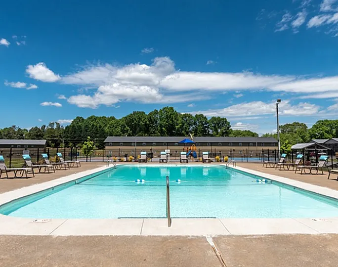Inviting outdoor pool with lounge chairs under a clear blue sky, surrounded by lush greenery.