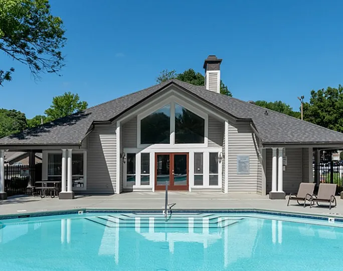 Inviting outdoor pool area with modern clubhouse and lounging chairs under a clear blue sky.