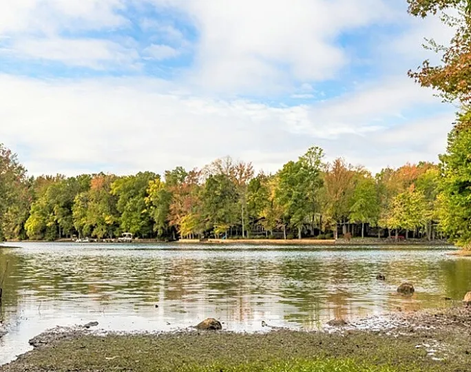 A tranquil lakeside view surrounded by lush green trees under a partly cloudy sky.