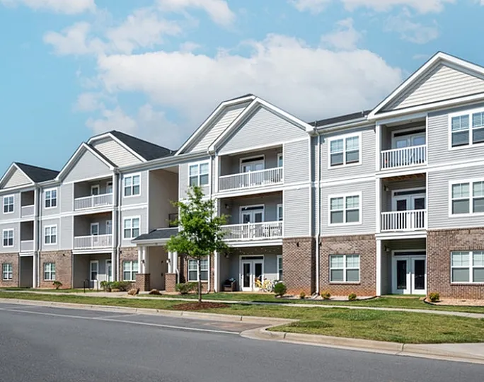Elegant three-story apartment building with balconies and well-maintained landscaping under a bright blue sky.