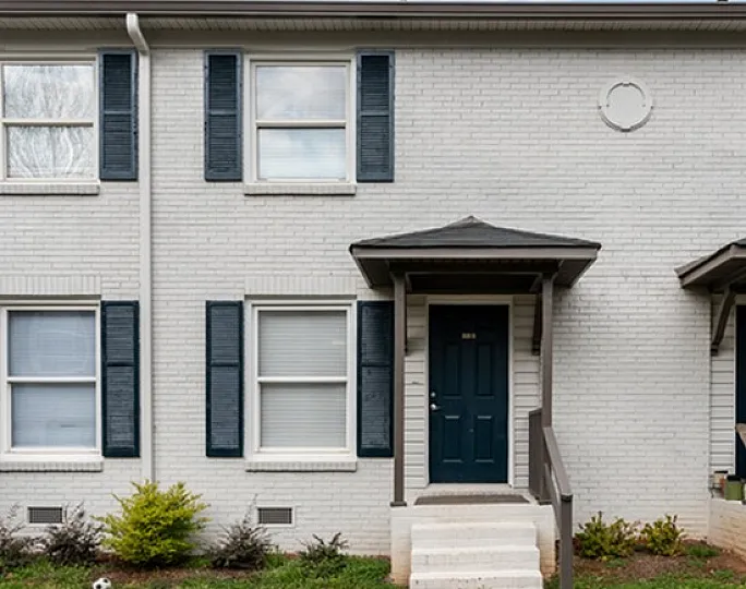 Inviting two-story townhouse with white brick facade and elegant blue shutters.