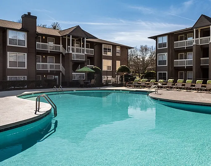 Inviting apartment complex featuring a large, sparkling pool with lounge chairs and modern architecture.