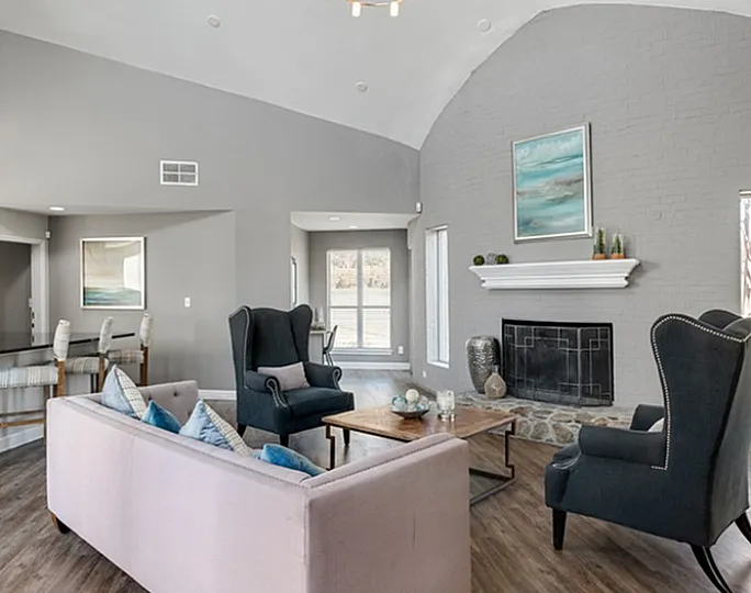 Elegant living room featuring a light pink sofa, two dark wingback chairs, a cozy fireplace, and modern decor.