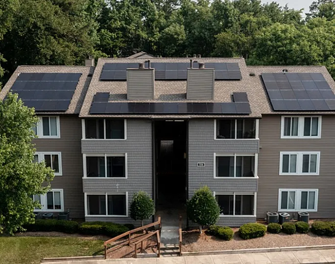 Modern apartment building with solar panels on the roof, surrounded by lush greenery.