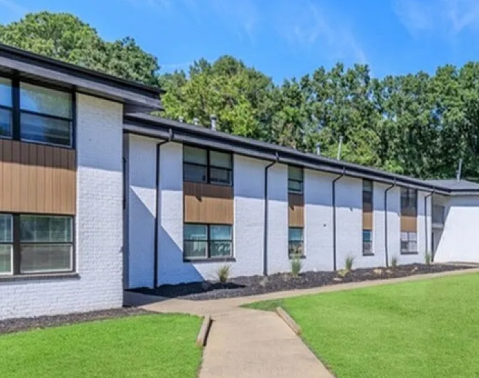 Charming apartment building with sleek modern design, surrounded by lush greenery and clear blue skies.
