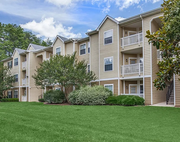 Charming and spacious apartment complex with serene balconies, manicured lawns, and lush greenery under a bright blue sky.
