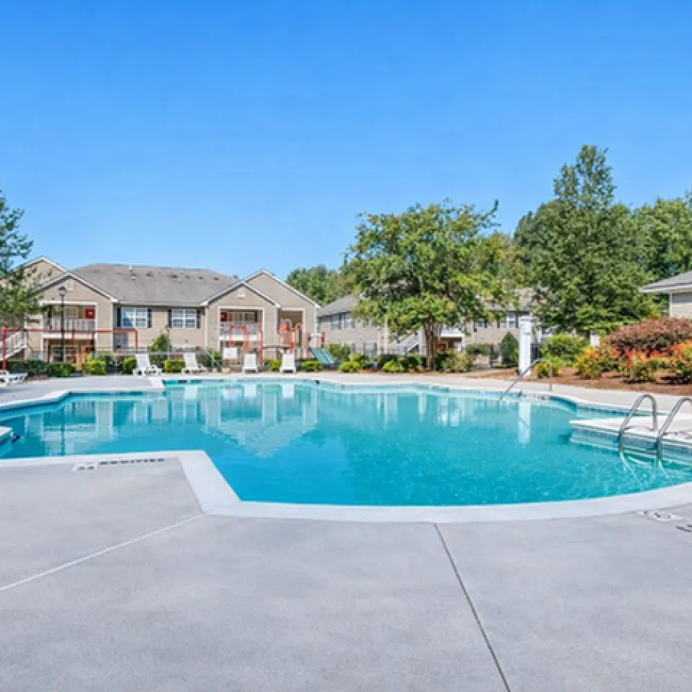 Inviting apartment community with a sparkling swimming pool surrounded by lush greenery and charming residences.