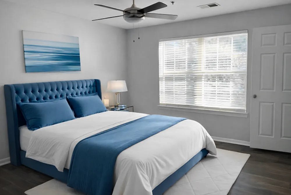 Elegant bedroom with a plush blue tufted bed, modern ceiling fan, and ample natural light from large windows.