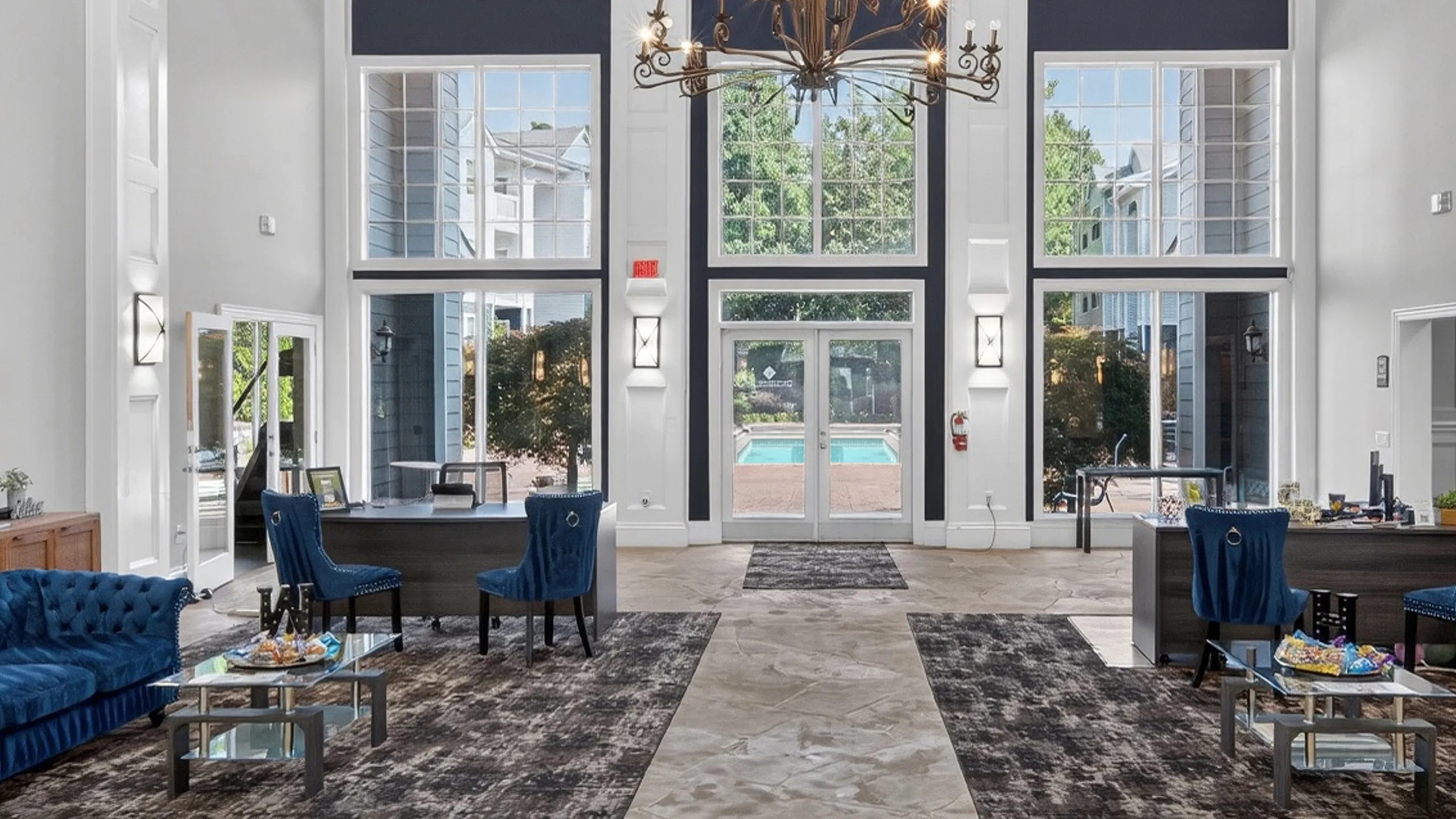 Luxurious open-concept lobby with elegant chandeliers, plush blue seating, and expansive windows showcasing a pool view.