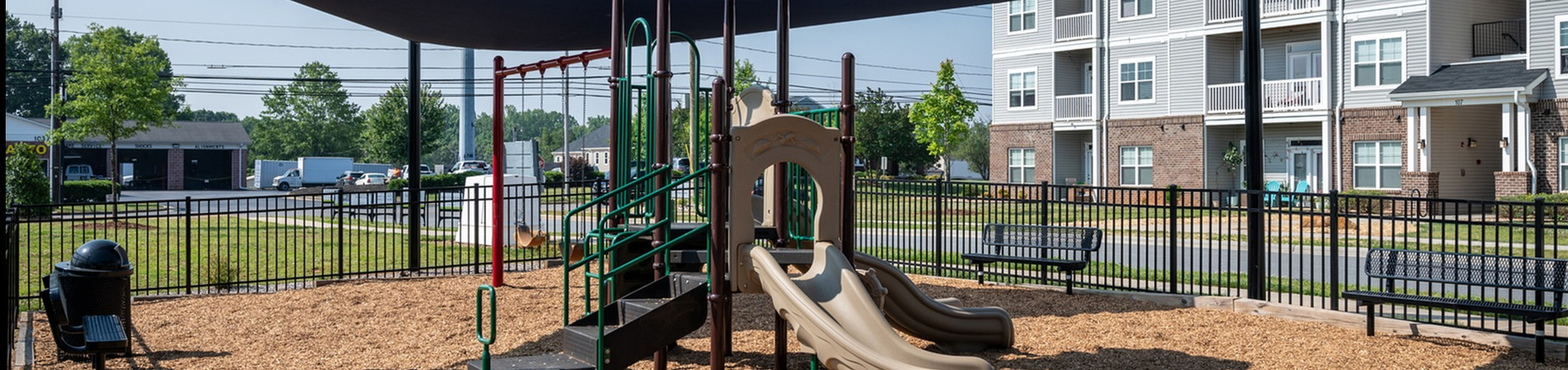 Inviting playground with slides and climbing equipment under shaded canopies, set in a family-friendly apartment complex.