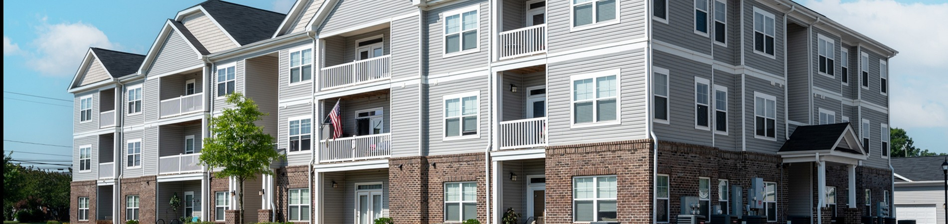 Charming three-story apartment building with modern siding, inviting balconies, and lush landscaping in a serene neighborhood setting.