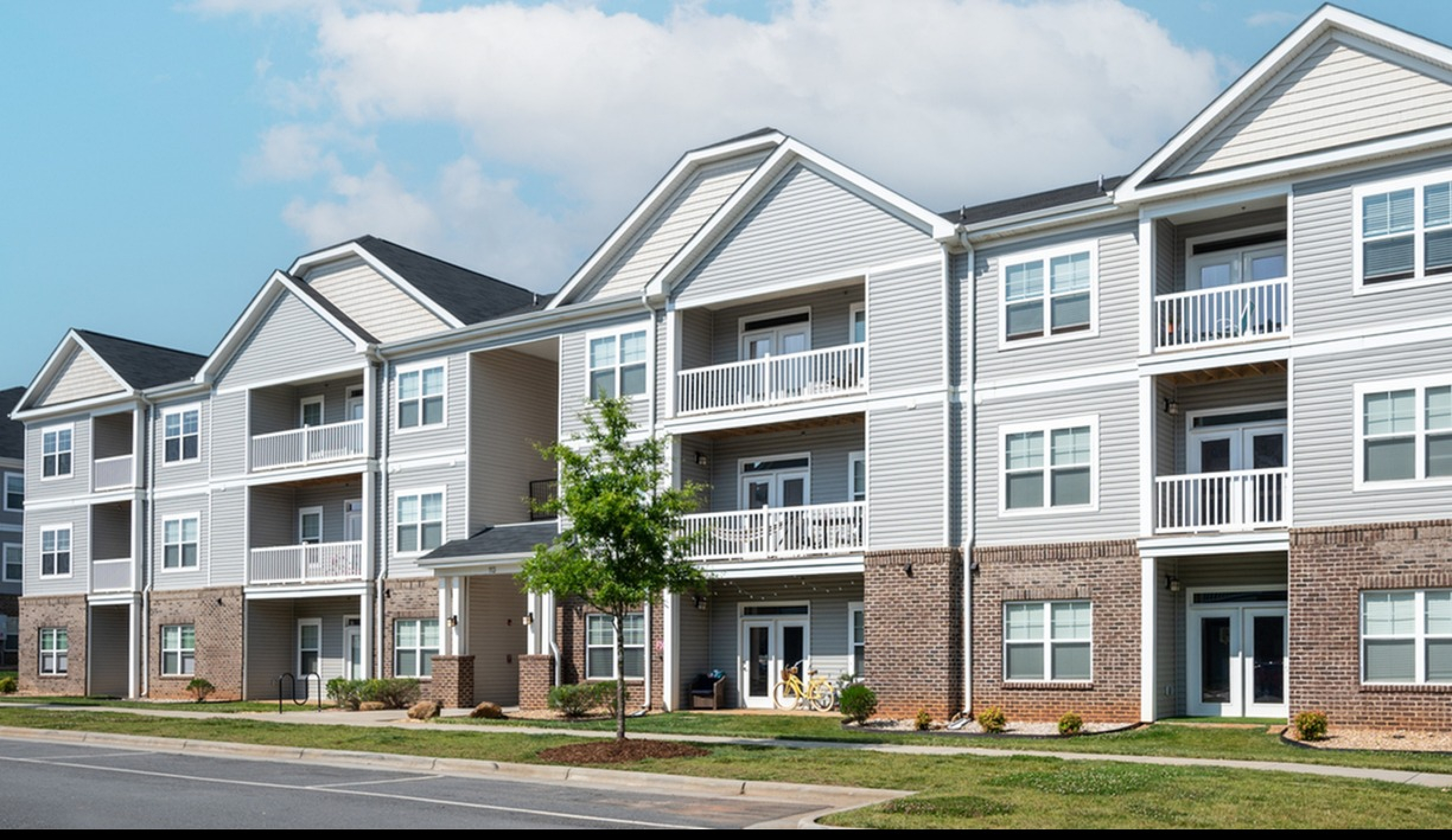 Modern three-story apartment complex with stylish balconies and pristine landscaping under a clear, blue sky.