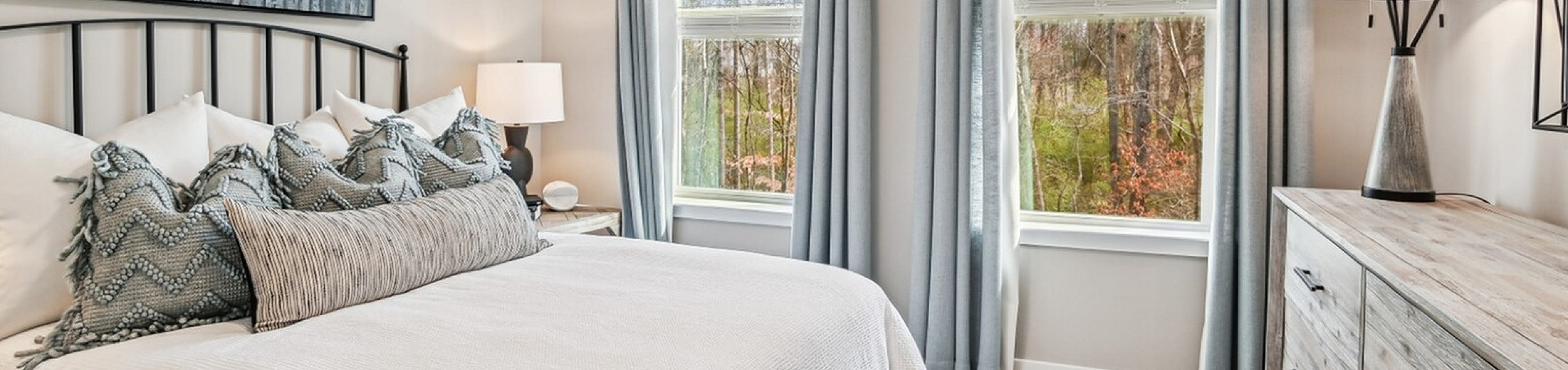 Bright and inviting bedroom with modern decor, large windows, elegant gray curtains, and cozy bedding.