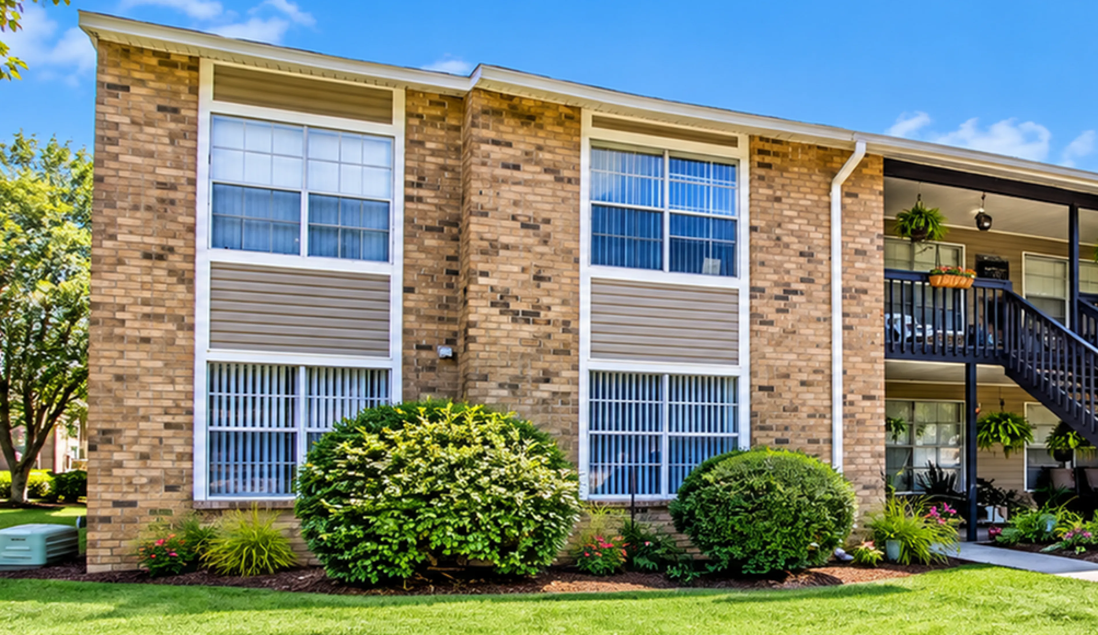 Charming apartment building with lush greenery, showcasing a welcoming exterior with vibrant landscaping and a sunny, blue sky overhead.
