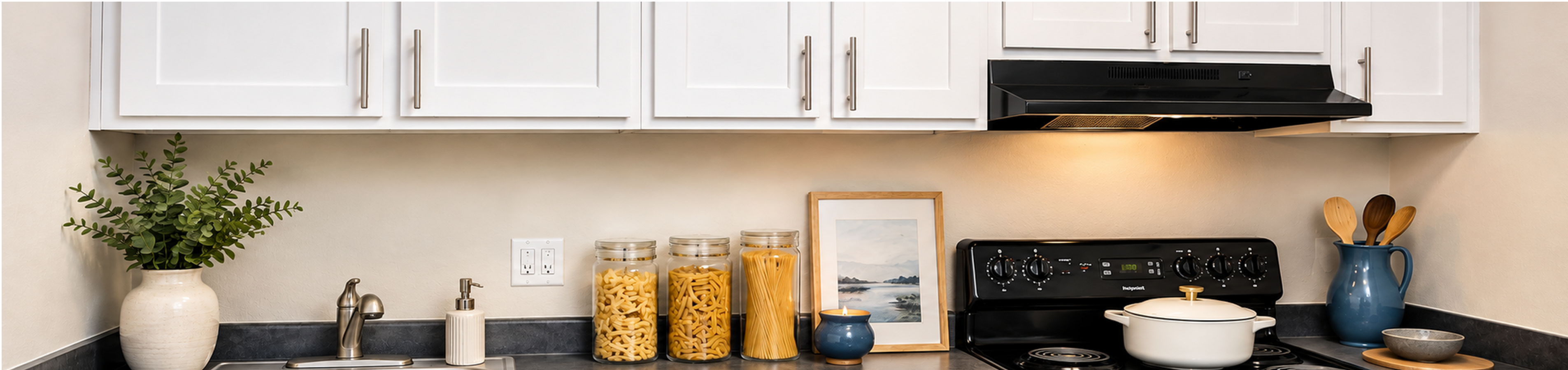 Chic kitchen interior with sleek countertops, modern white cabinetry, and stylish decor, featuring pasta jars and elegant kitchenware.