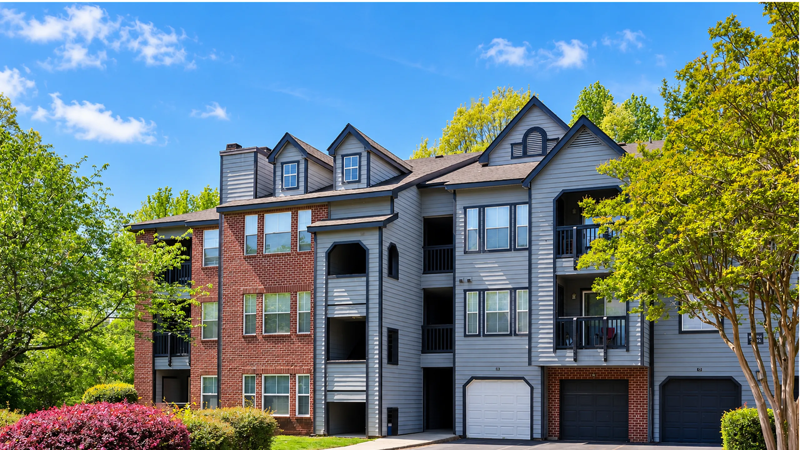Charming apartment building featuring modern architecture with brick and siding accents, surrounded by lush greenery and vibrant landscaping.