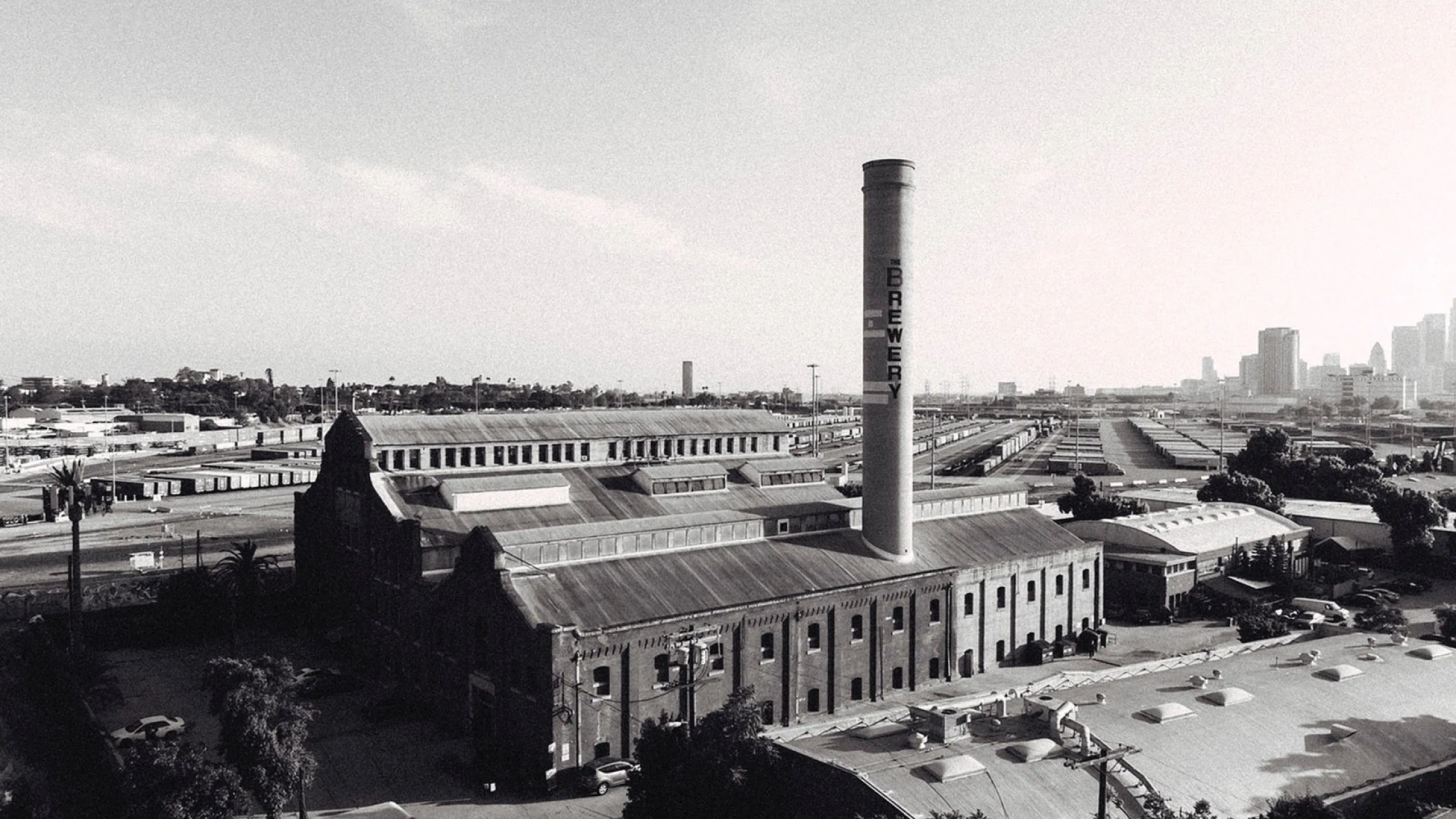 Historic industrial architecture with a prominent brewery chimney, vibrant urban skyline in the background.