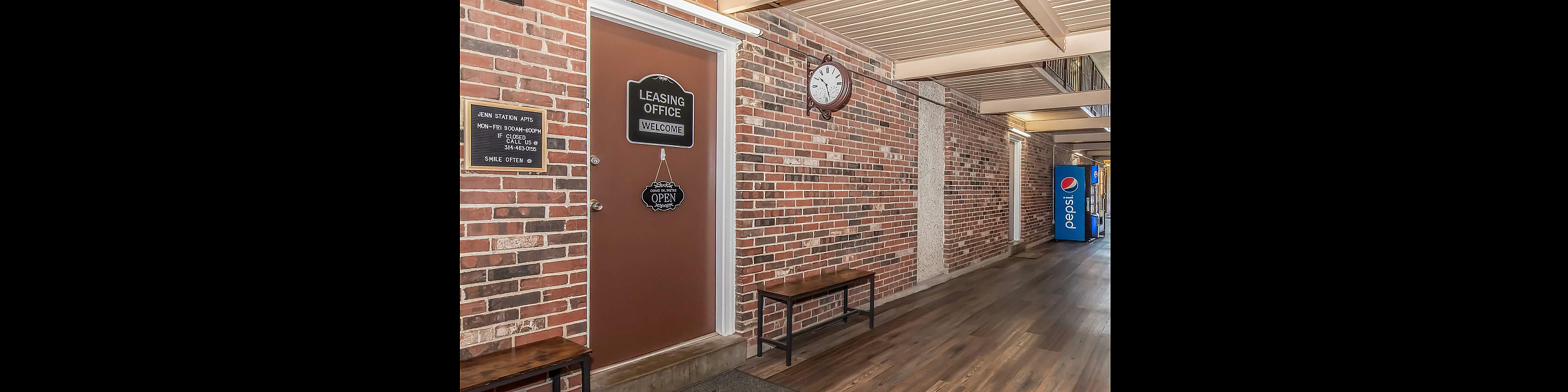 Inviting leasing office entrance with charming brick walls, welcoming signage, and convenient seating, promising a cozy community vibe.