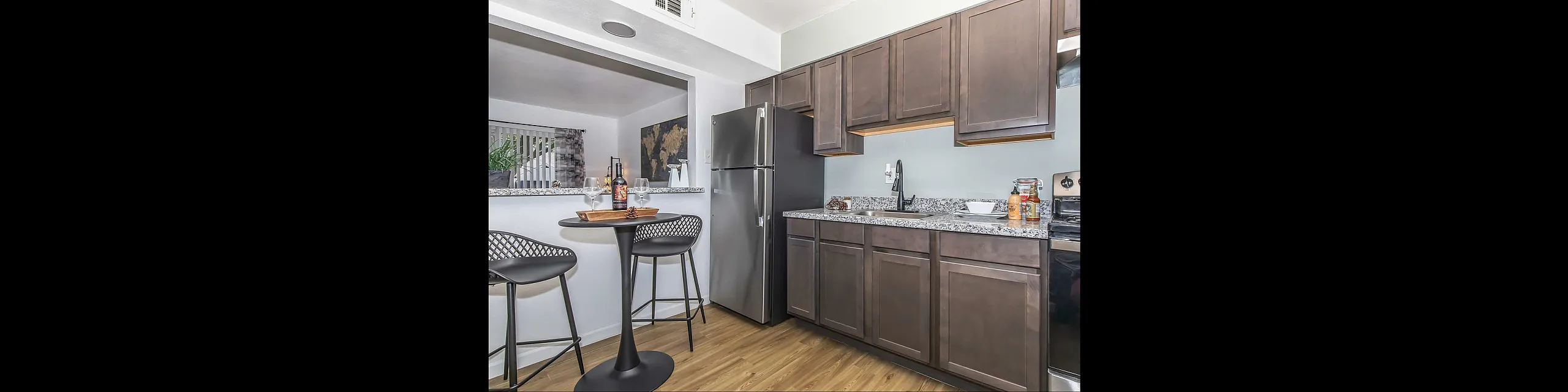 Modern kitchen with elegant dark wood cabinets, sleek granite countertops, and a cozy breakfast nook featuring stylish bar stools and a wine setup.