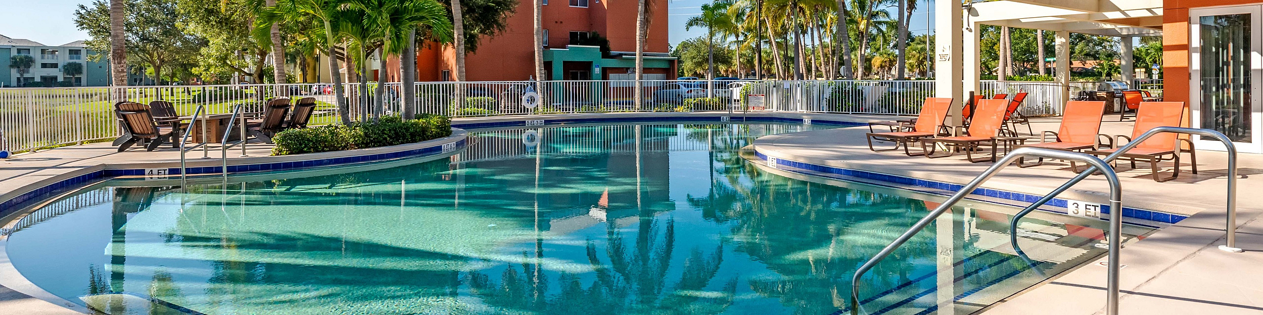 Luxurious resort-style pool area with palm trees and vibrant sun loungers, perfect for relaxation and leisure under clear blue skies.