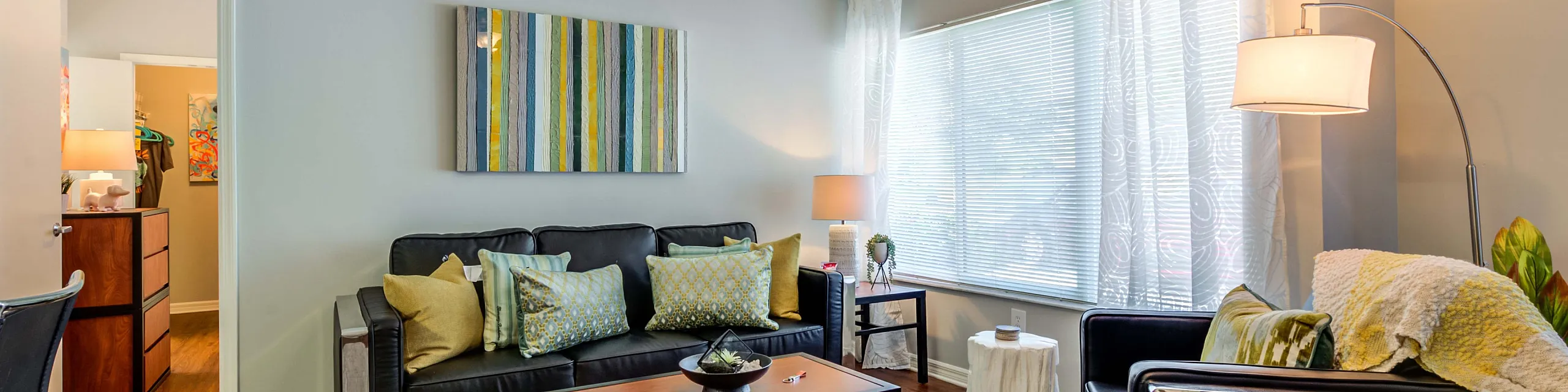 Bright, contemporary living room with stylish decor, featuring a plush black sofa, chic armchair, and modern coffee table under a warm ceiling light.