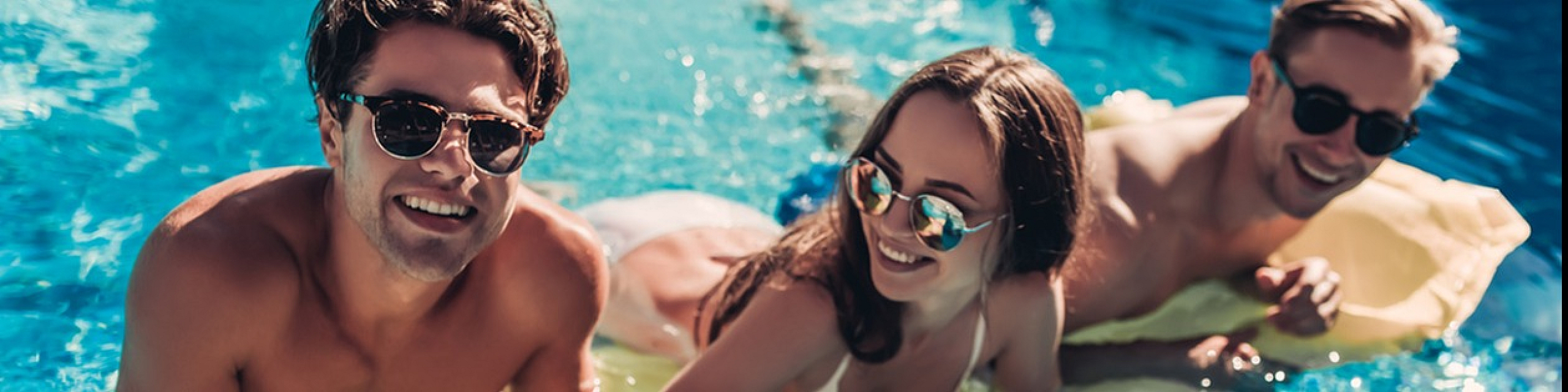 Vibrant poolside relaxation with friends enjoying a sunny day on a bright inflatable mat in crystal clear water.