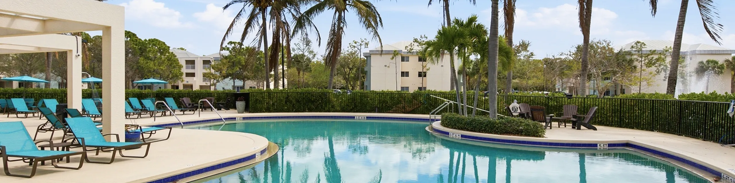 Luxurious apartment complex featuring a stunning outdoor pool with palm trees and comfortable lounge chairs, perfect for relaxation and enjoying sunny days.