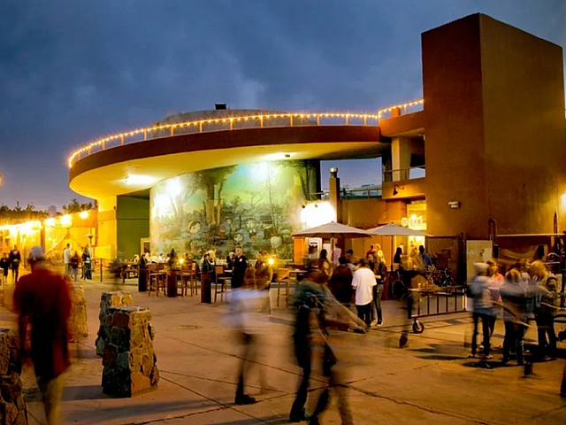 Vibrant evening scene at a lively outdoor plaza with modern architecture, atmospheric lighting, and bustling crowds enjoying the ambiance.