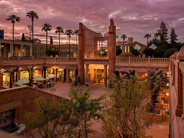 Inviting outdoor courtyard with elegant architecture and palm trees, set aglow beneath a stunning sunset sky.