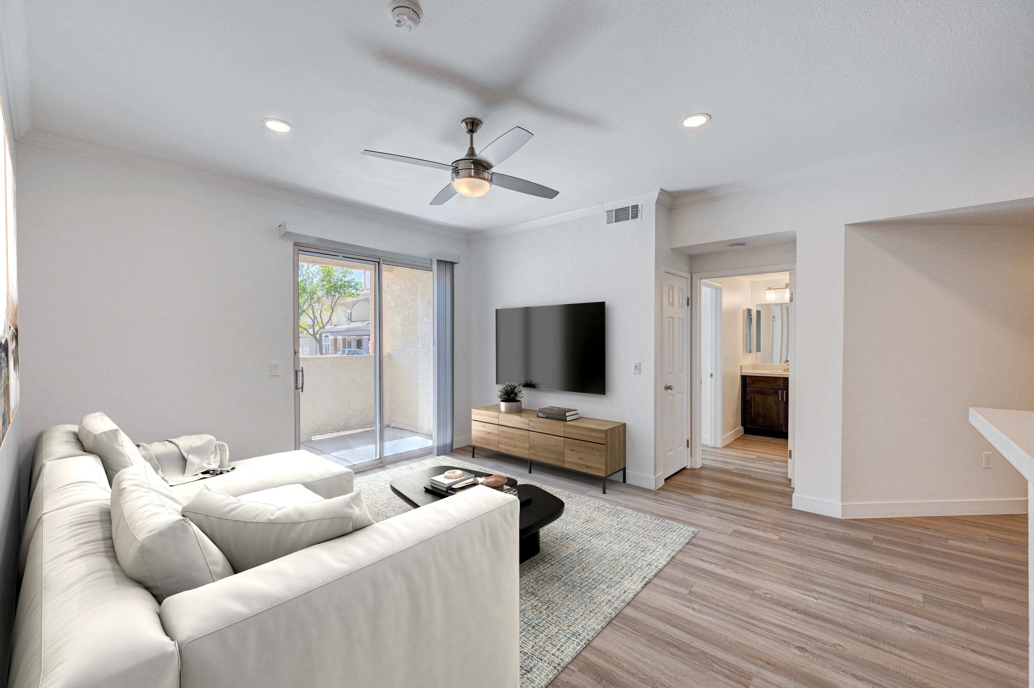 Modern living room with sleek hardwood floors, plush white sectional sofa, and large glass doors leading to a serene balcony.