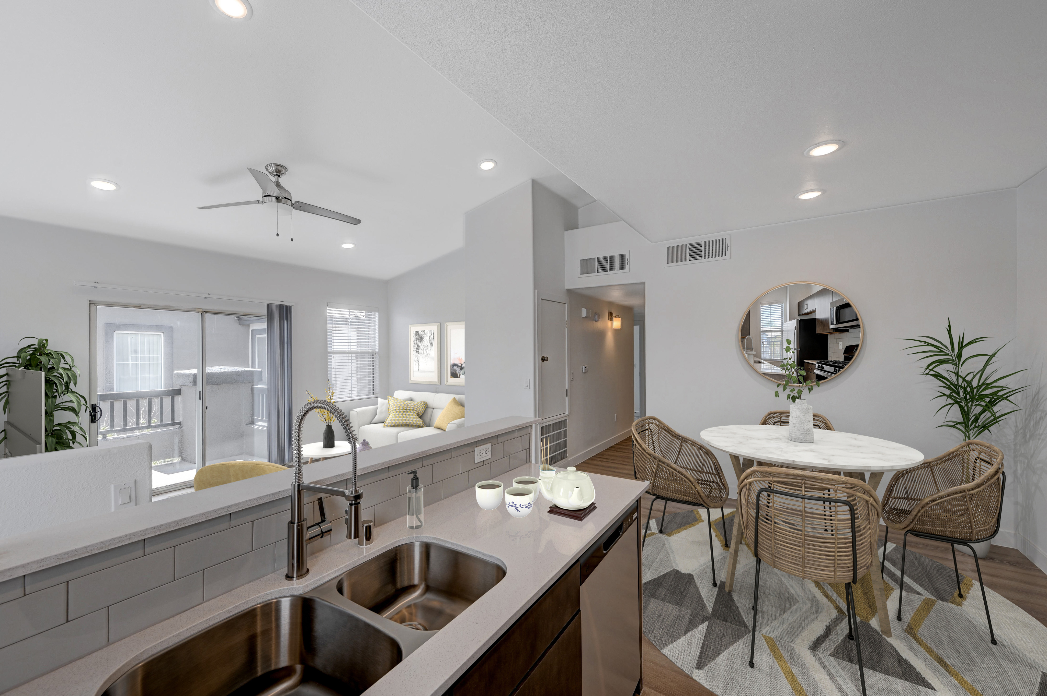 Bright and airy open-concept kitchen and dining area with modern finishes and natural lighting, featuring a sleek sink and wicker dining chairs.
