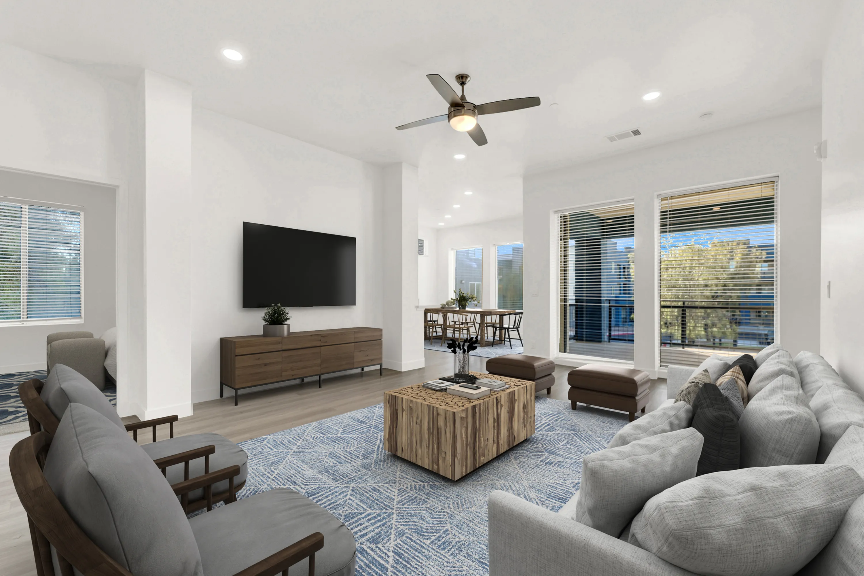 Bright and spacious living room with modern furnishings, featuring a large sectional sofa, stylish coffee table, and a ceiling fan, opening into a dining area with natural light streaming through broad windows.